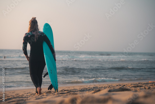 Fotografija Surfing woman carrying surf board, wetsuit beach scene