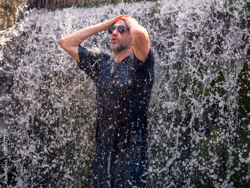 Photos A man is standing in a waterfall, with his arms outstretched