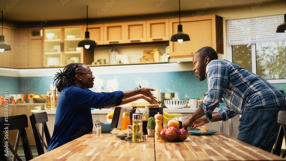 Fototapeta premium Black woman eating alone after her boyfriend is rushing to leave for work, running late and skipping breakfast. Morning routine in a hurry for man being late for his office job, lifestyle.