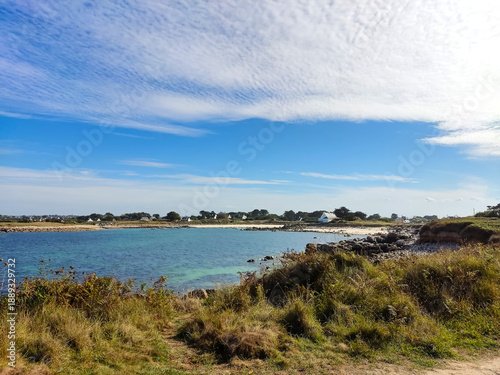 Wallpaper Mural View across a beach with grass and clear water under a blue sky, calm coastal landscape with natural shoreline and open horizon. Torontodigital.ca