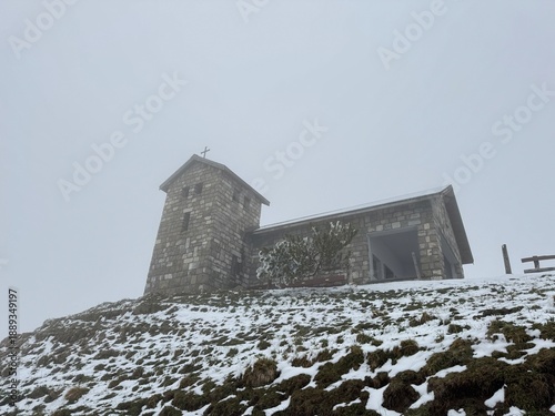 Snow falls on a stone church near the top of a mountain in a cold, cloudy setting during winter months in a remote location