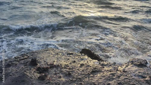 In the Aegean Sea, the sea crashes hard against the rocks in windy and choppy weather. A cloudy sunset in the sky.	
