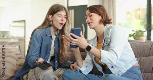 Wallpaper Mural Female friends sitting on couch, right friend showing blue phone case, left holding remote laughing Torontodigital.ca