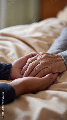 Close-up of a caregiver gently holding the hands of an elderly person lying in bed, expressing comfort and emotional support.
