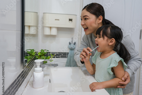 mother teaching girl child to brushing teeth in bathroom
