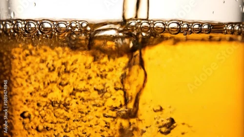 Dynamic close-up shot of a golden beverage being poured, showcasing effervescent bubbles and frothy foam