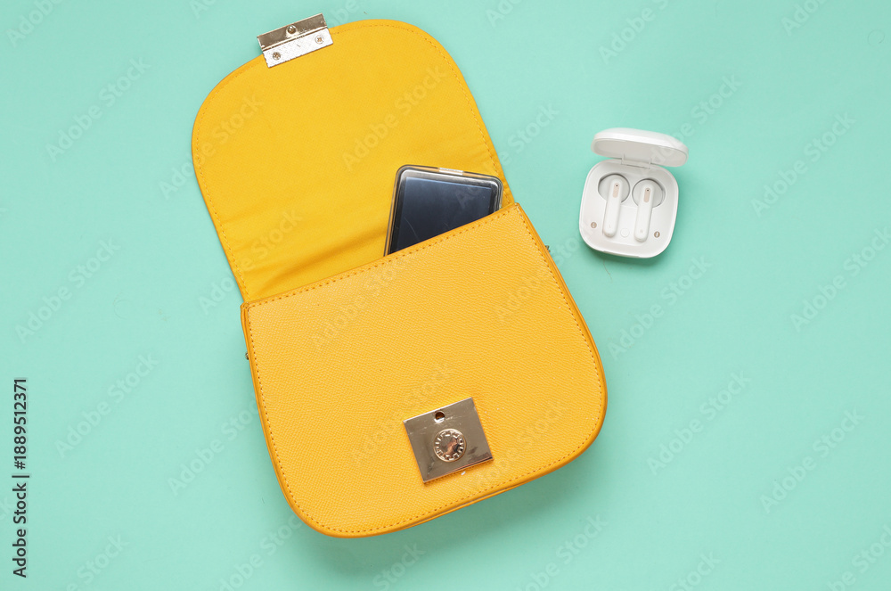 Fototapeta premium Women's yellow bag with wireless earphones case on a blue background