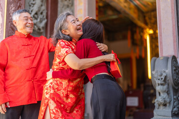 Asian grandparents receiving red envelope from young woman at chinese temple, joyful moment of giving during lunar new year celebration, showing love, family connection and festive cultural tradition