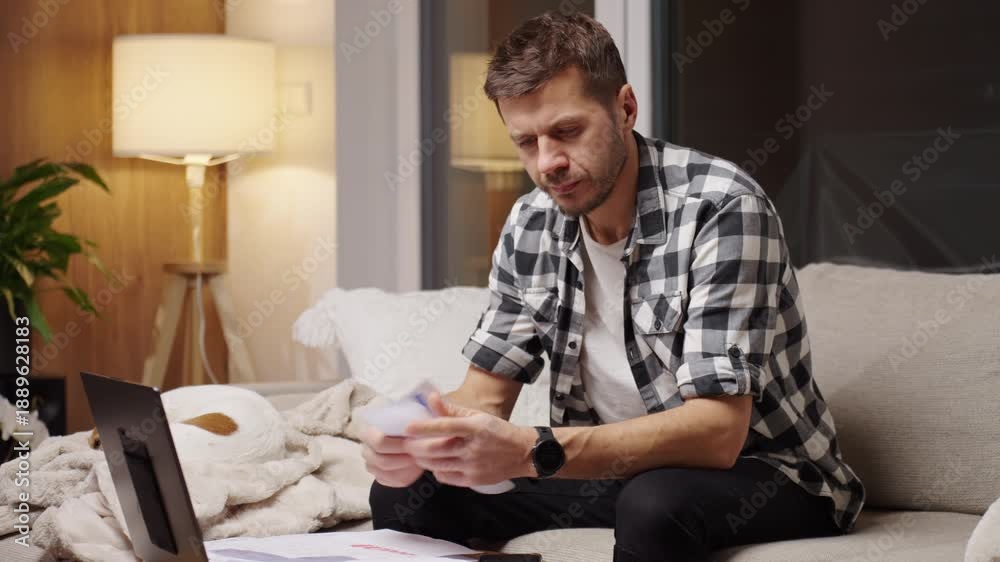 custom made wallpaper toronto digitalMan sitting on couch at home holding paper bills and financial documents near a laptop. Concept of financial pressure from increasing household expenses and difficulty managing payments.