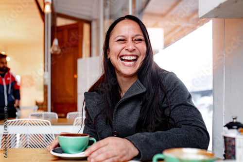Happy Maori woman sitting at cafe table with a coffee