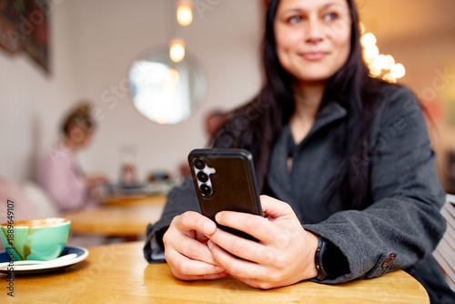 Maori woman sitting at cafe table with a coffee holding her phone