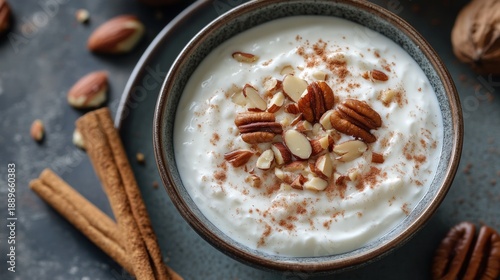 Close-up of creamy yogurt in a bowl, topped with nuts and cinnamon, with cinnamon sticks