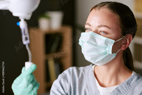 Cuadro en lienzo Caucasian young adult woman wearing medical mask and gloves adjusting intravenou