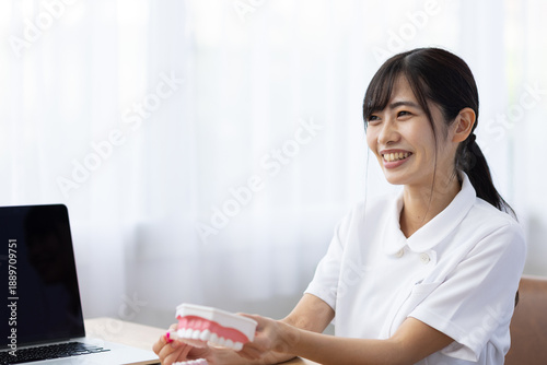 Fotografi Smiling Young Woman in White Uniform Teaching Tooth Brushing with Dental Model