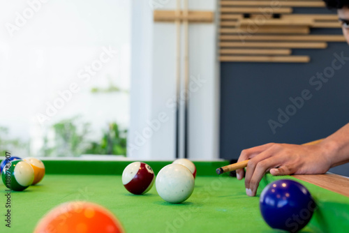 Man positioning cue stick toward cue ball on pool table, short-sleeve shirt, copy space
