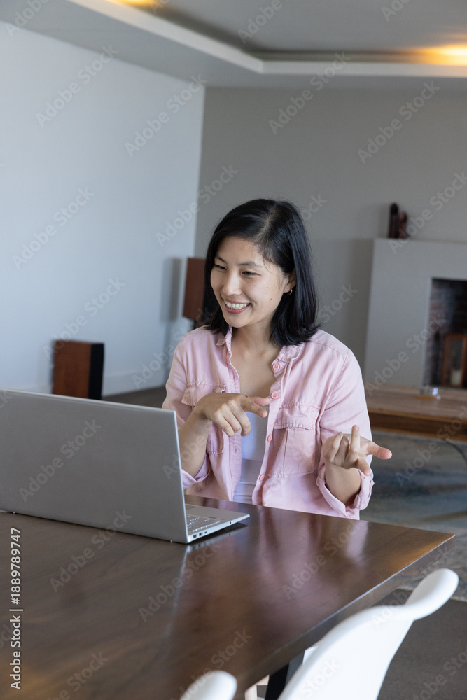 Obraz premium Asian woman pointing at laptop screen while sitting at wooden table at home wearing shirt