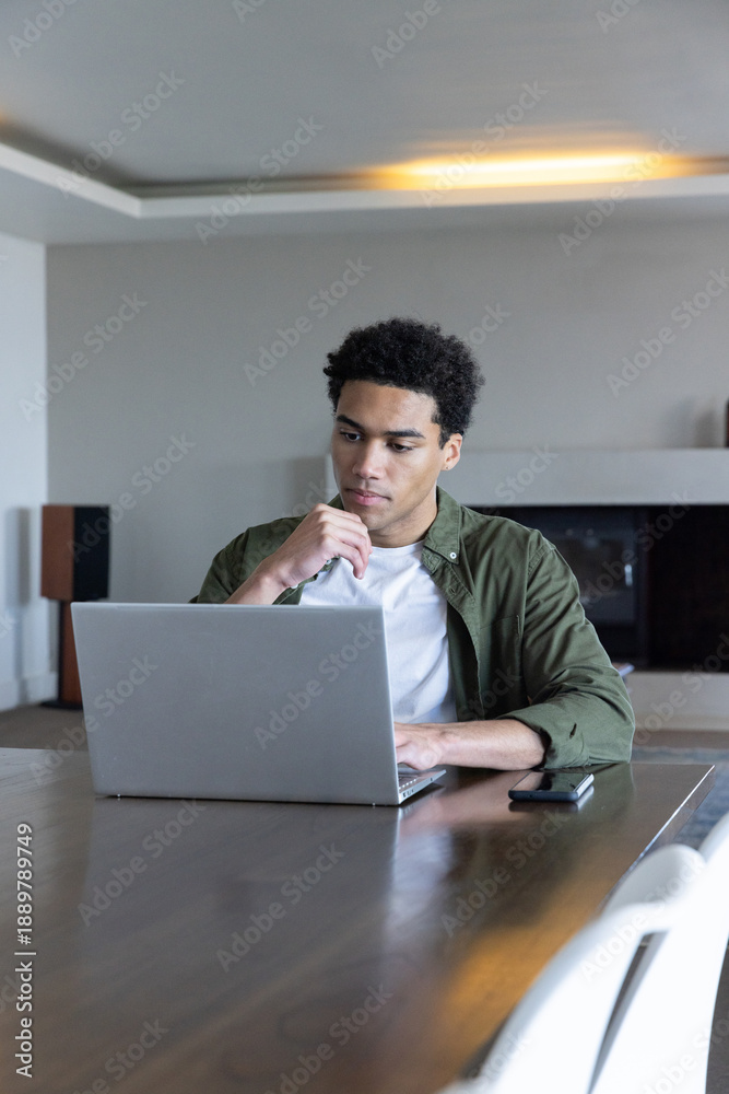 Fototapeta premium African american man working on laptop at table in living room with smartphone