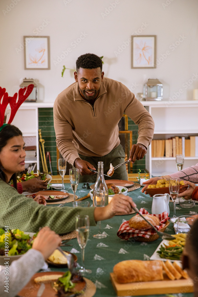 Fototapeta premium African american man carving roasted bird with knife and fork in home dining room