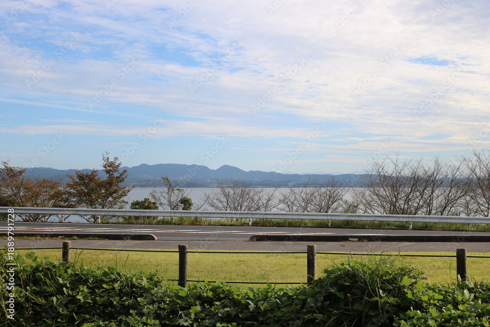 Fototapeta premium Wide Sky and Lakeside Road Landscape with Meadow and Mountains