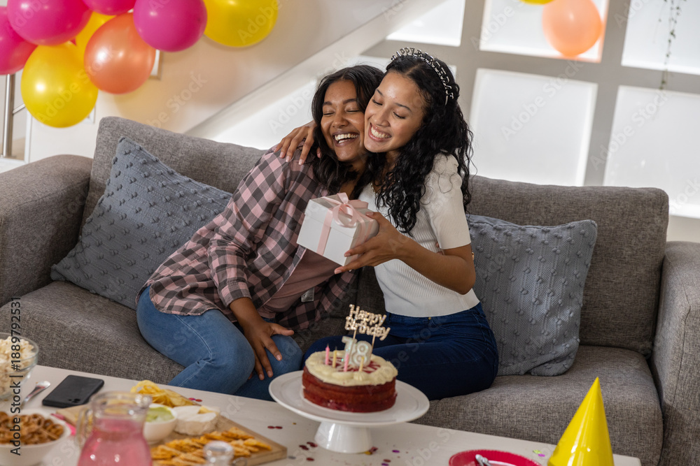 Fototapeta premium Diverse mom and teenage daughter hugging and celebrating birthday in living room with cake