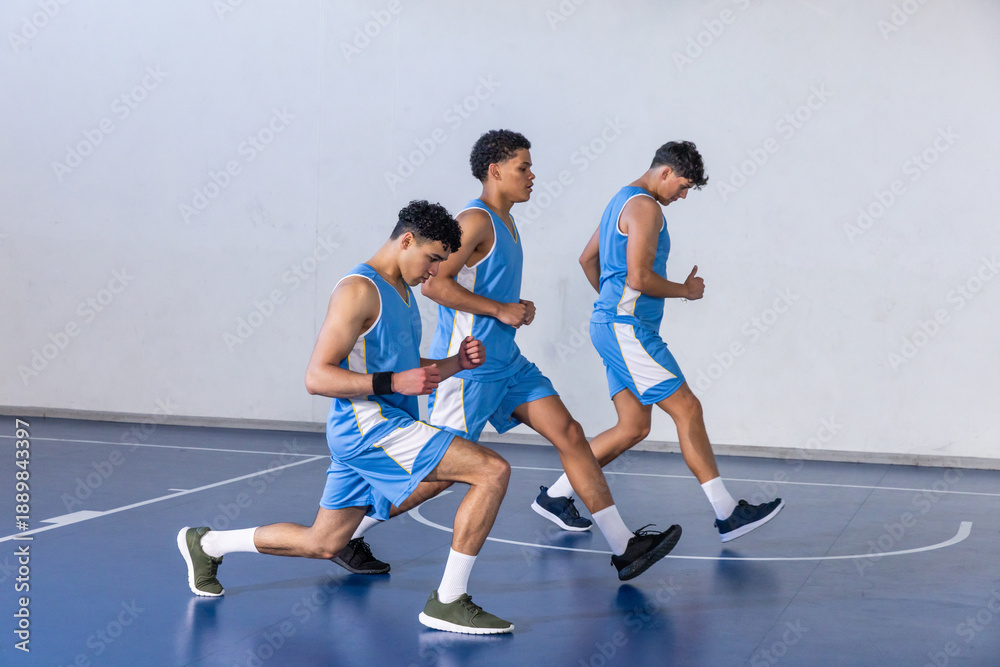 Fototapeta premium African american teenage basketball teammates performing forward lunges on court in uniforms