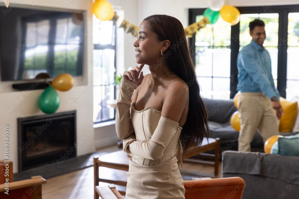 Fototapeta premium Diverse couple standing in living room with green balloons, banner, showcasing beige dress