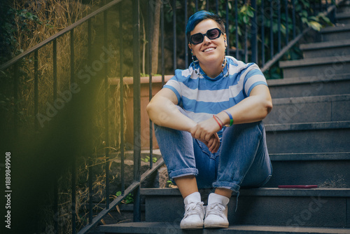 Фотография Smiling non-binary person with blue hair and sunglasses sitting on outdoor stair