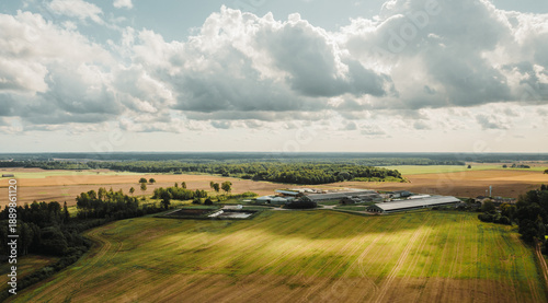 Drone view of large agricultural farm complex surrounded by green and golden fields. Modern rural infrastructure, food production facilities, and sustainable farming landscape.