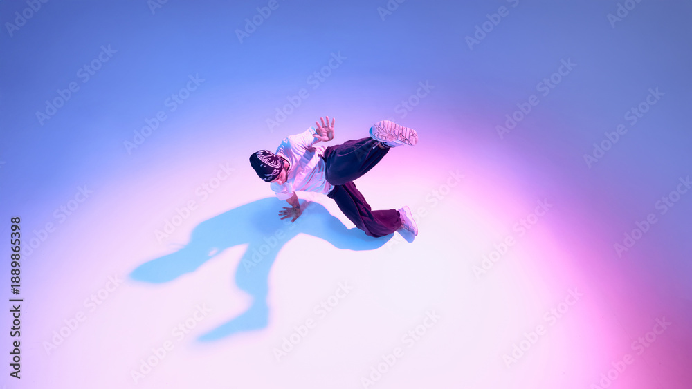 Obraz premium Breakdance dancer performing dynamic floor move with extended leg on gradient background. Concept of street dance expression, athletic performance, body mechanics, and modern lifestyle visuals.