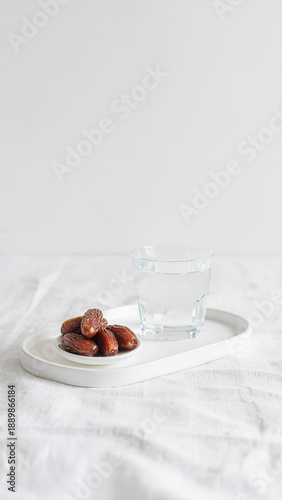 A wide view of essential sunnah food for breaking the fast, featuring premium dates and a clear glass of water on a minimalist white table background.