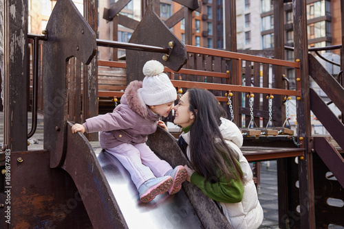 Mother and daughter touching noses, playing together on a playground slide