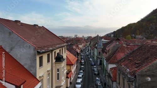 1 november 2024, Brașov, Romania. Forward drone in street between buildings, rooftops towards hill with forest, trees in autumn colors, brasov city. Touristic must-see destination.