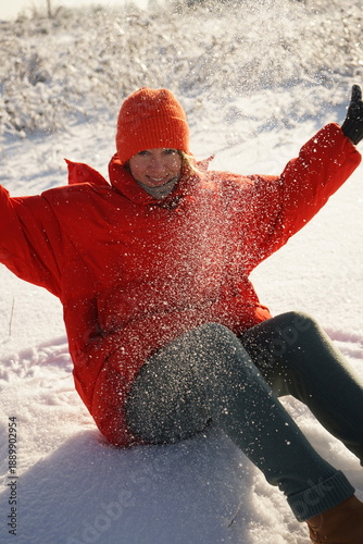 A girl throws snow over herself against the sun in a red jacket