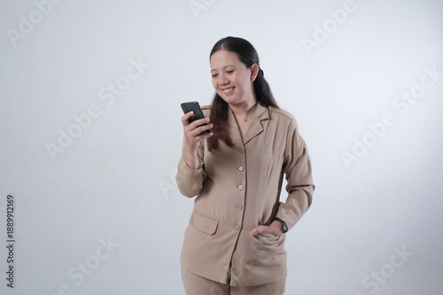 Fotografie Indonesian female civil servant wearing official ASN uniform smiling while checking smartphone in studio