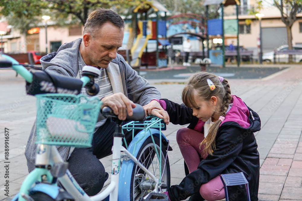 Obraz premium Father and nine year old child pumping wheels of a kid's bicycle outdoors, family activity and childhood
