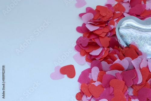 A mirrored metal heart on a white background surrounded by red, pink, and purple paper hearts — a romantic composition.