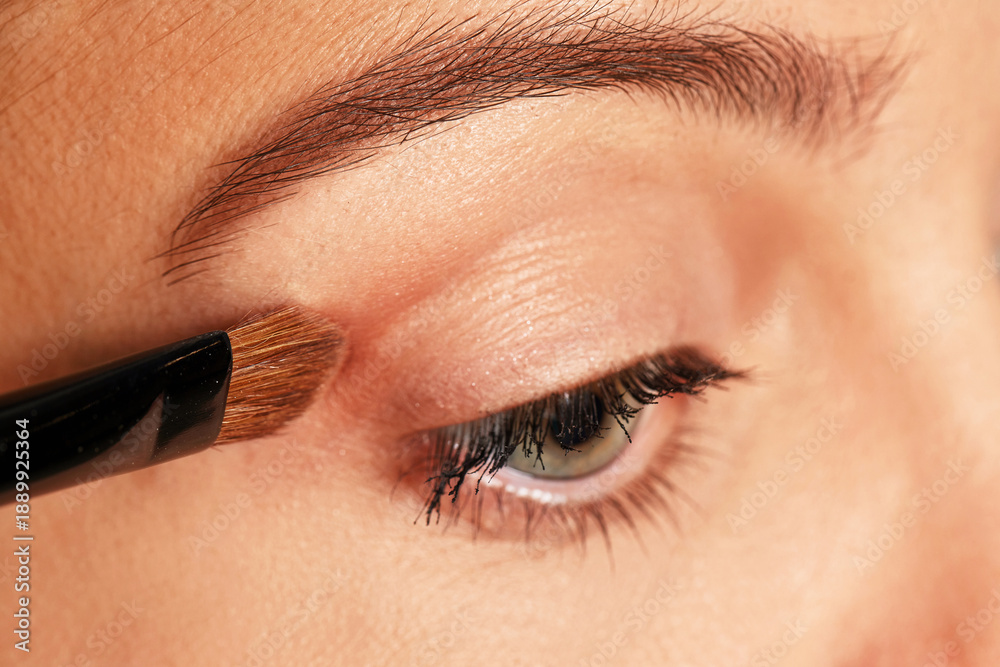 Naklejka premium Woman applying cosmetic eyeshadow to her eye using a brush