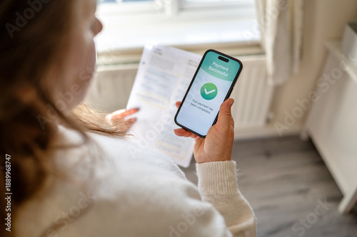 Foto Utility bills successfully paid using mobile banking app on smartphone while holding paper invoice at home