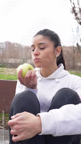 Athletic woman in sportswear taking a break and eating a fresh green apple in a park
