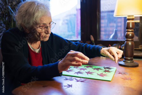 Tableau sur toile Elderly woman creates herbarium with colorful leaves on a wooden table