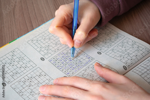 Top view of female hands solving a sudoku puzzle in a paper magazine with a blue pen