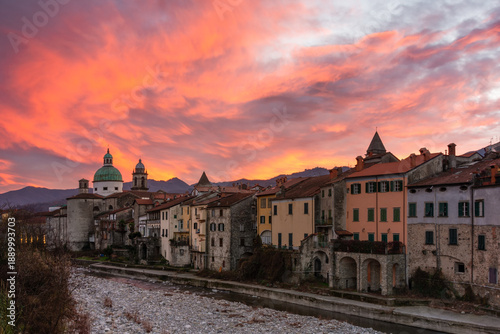 View of the old architecture glows under the vivid orange and pink sky, reflected in the dry riverbed, creating a tranquil yet vibrant scene, Pontremoli, Tuscany, Italy.