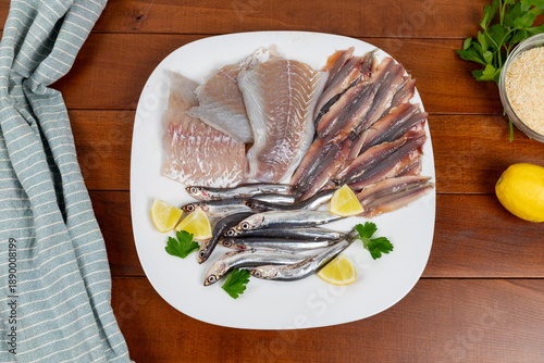 Raw mixed fish on a white plate. Fillets of saithe and anchovies. Flat lay.
