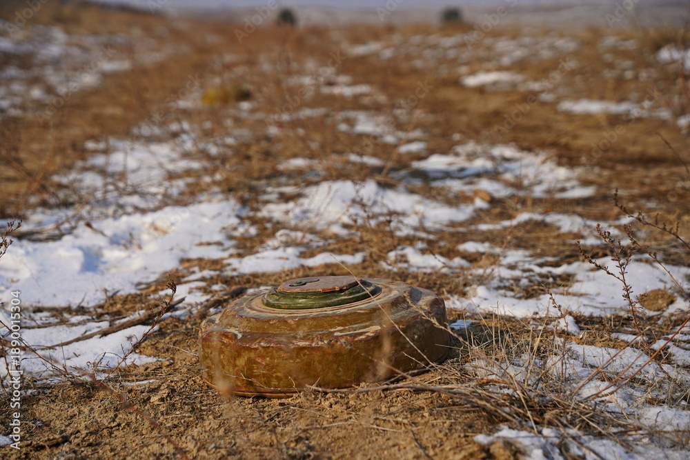 Naklejka premium An anti-personnel mine is lying on the ground among the soil and snow.