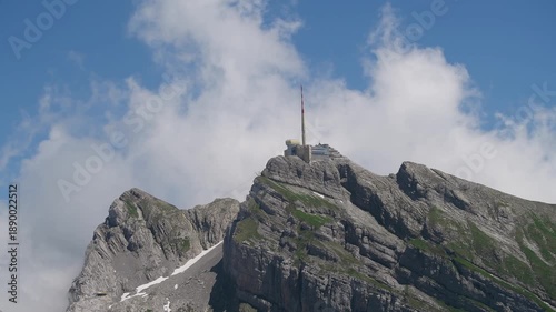 Mountain peak with tower visible against blue sky and clouds during daytime