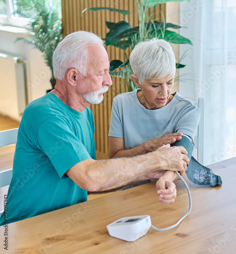 Senior man checks blood pressure of woman in home kitchen during morning