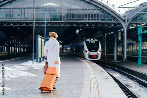 Foto Caucasian redhead woman walking with suitcase toward arriving train