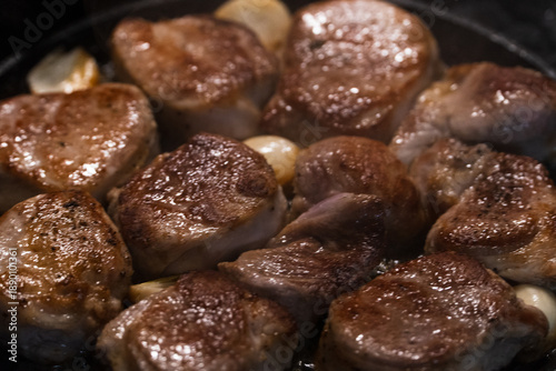 Foto Several meaty pork pieces are fried in a frying pan with garlic and spices, emitting steam and a spicy aroma, and glistening from the released fat