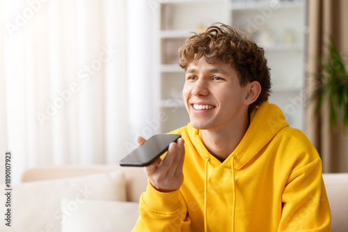 Photos Teen guy using smartphone at home, smiling while speaking on voice call, dressed