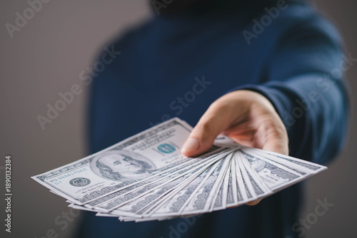 Photos Hand holding and giving cash money in US dollar bills, representing financial transaction, cash payment, income, profit, salary, business finance, investment return, and economic exchange concept